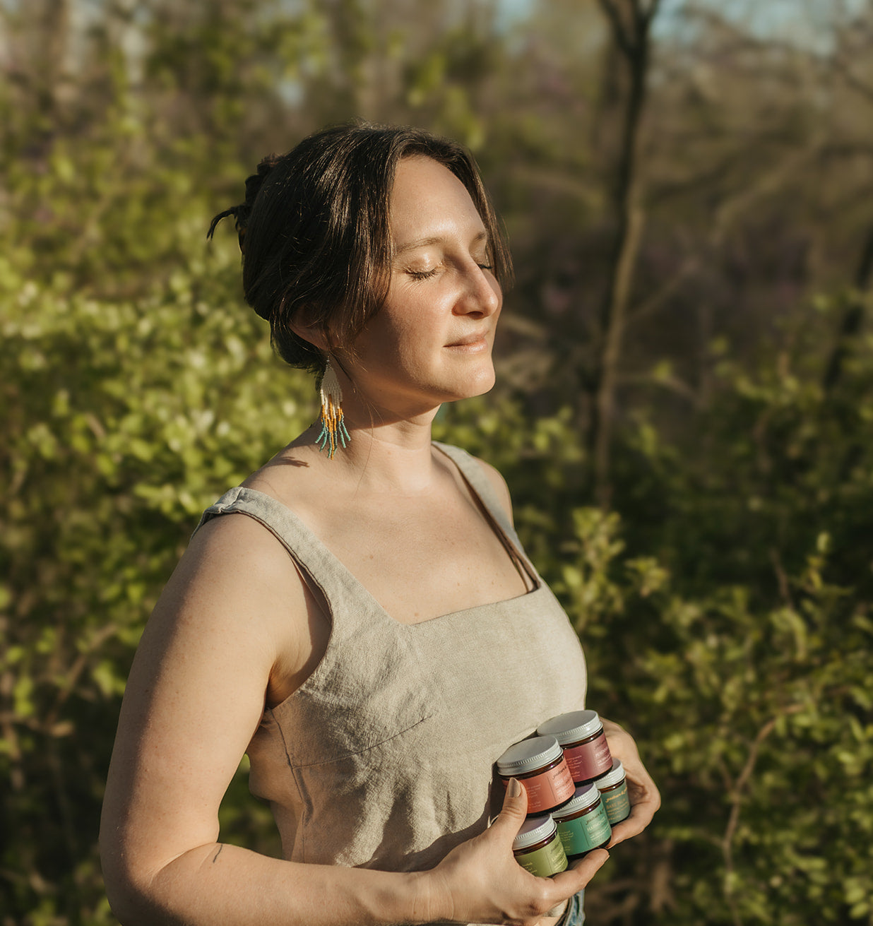 Woman holding colorful jars outdoors with greenery in the background