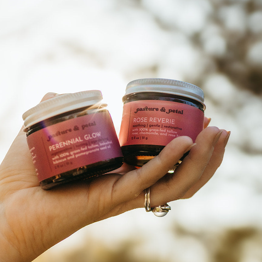 Hand holding two small jars with pink labels against a blurred natural background